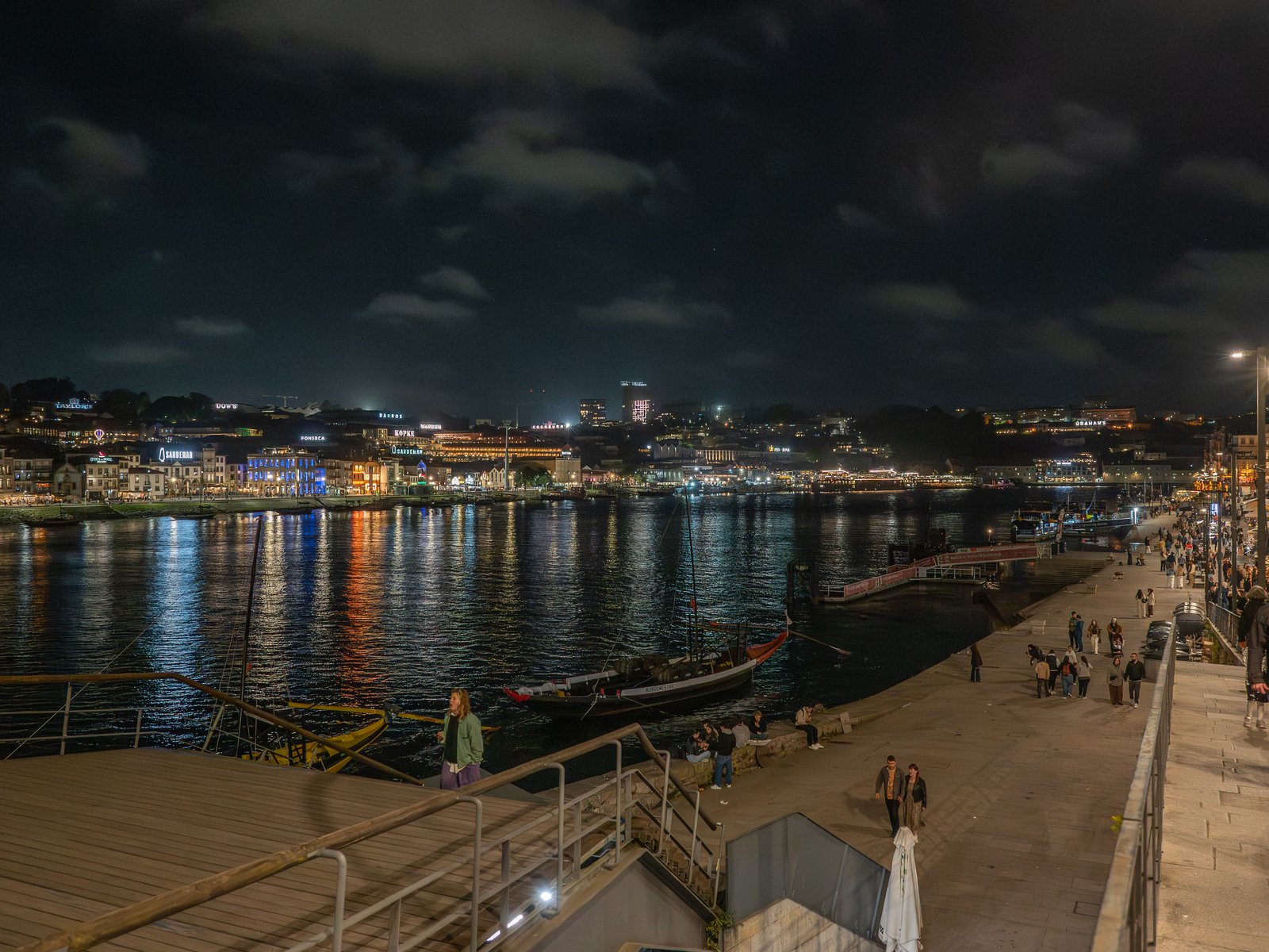 A riverside city promenade lit up at night with lights reflecting on the water